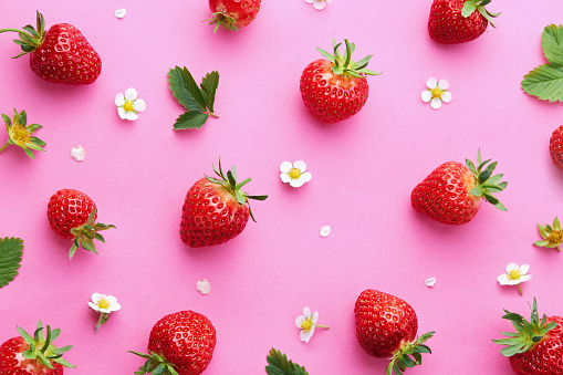 Fresh red strawberries with flowers and leaves on pink background. Summer berries pattern.