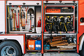 Fire truck with plastic canisters under metal nippers and tire jack with fire extinguisher near similar safety vests in garage
