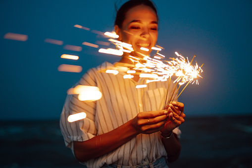 Glowing sparkles in hands. Women with Christmas sparklers on nature and twillight sky background. Holidays, vacation, relax and lifestyle concept.