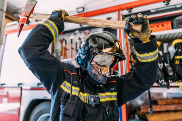 istock Side view of unrecognizable firefighter in uniform and hardhat carrying big used pickax with wooden handle while standing near fire truck with professional tools and safety vests 1338921982