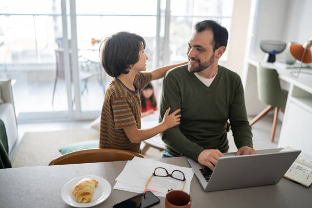istock Father working using laptop and talking with son at home 1338922534