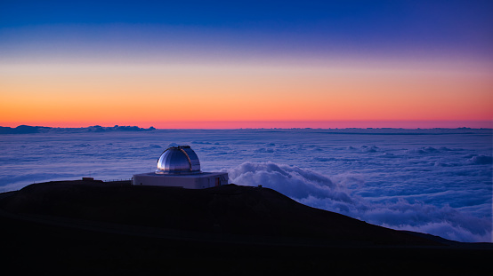 A deep space telescope at dusk above the clouds on Mauna Kea in Big Island, Hawaii.