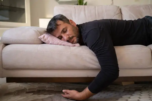 Photo of Man flopping down on sofa, needs rest at home