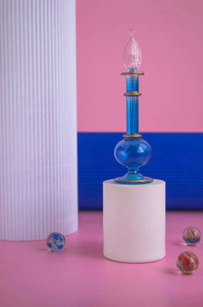Blue bottle with perfume on a white podium on a pink background and columns. Cosmetics presentation. Mockup of blue glass bottle with perfume or oil for advertising banner