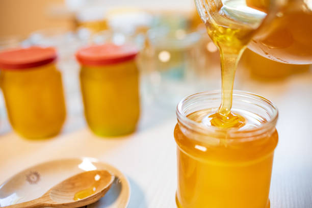 istock Someone pours honey into transparent jars on a white table 1338930242