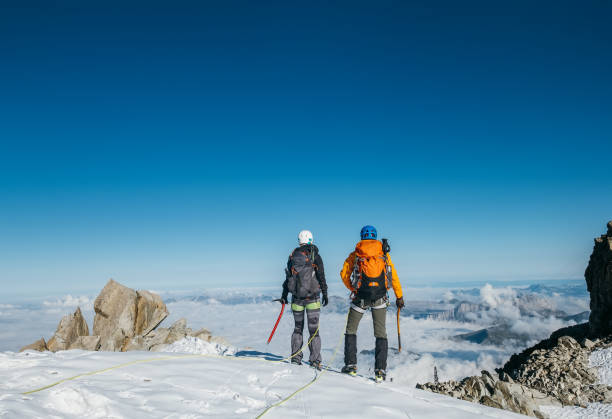 istock Couple connected team rope  with climbing harness dressed mountaineering clothes with backpacks and ice axes enjoying views ascending Mont Blanc (Monte Bianco) summit near Aiguille du Midi, France. 1338934370