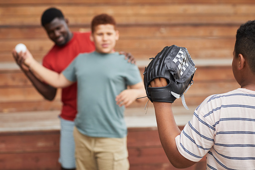 Over shoulder view of boy in baseball mitt catching ball thrown by brother with help of father