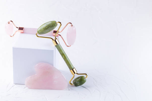 istock Rose quartz crystal and jade facial roller and massage tool Gua sha on white background, horizontal, copy space 1338939749