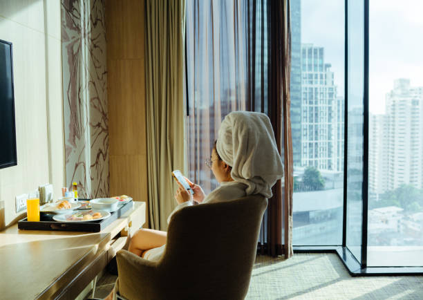 femme assise tenant une tasse de café et utilisant le téléphone - hotel wireless technology bedroom hotel room photos et images de collection