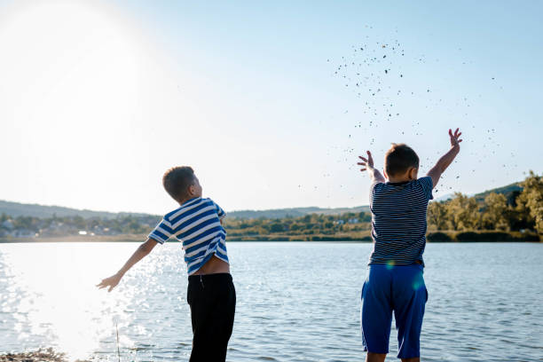 młodzi chłopcy bawiący się na jeziorze, wrzucający kamienie do wody. - throwing stone little boys child zdjęcia i obrazy z banku zdjęć