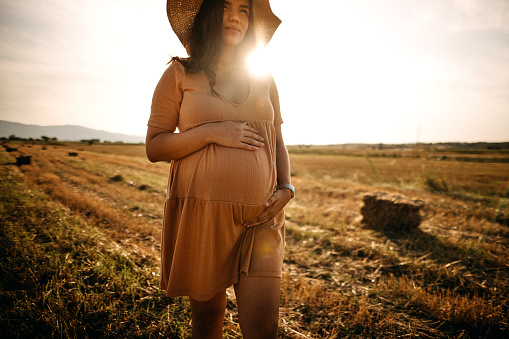 Young pregnant woman holding her stomach, relaxing in meadow