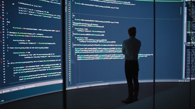 High-Tech Startup Concept: Innovative Male Software Engineer Standing, Doing Big Data Analysis on Wall Screen Showing Porgramming Code. Developing Futuristic e-Commerce App with Machine Learning. Full