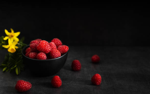 red raspberry in a black bowl on a dark background.