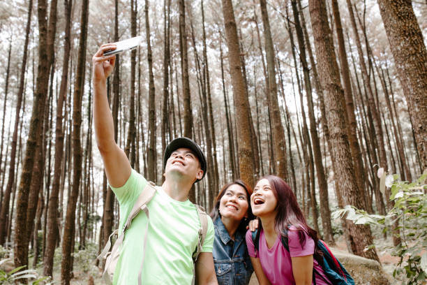 istock Three asian friends taking smartphone selfie during walking in the forest 1338958644