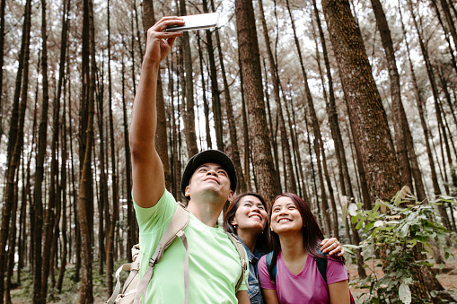 Three asian friends taking smartphone selfie during walking in the forest