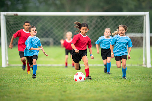 Soccer ball, playing together. Kids are having fun on the field at daytime.