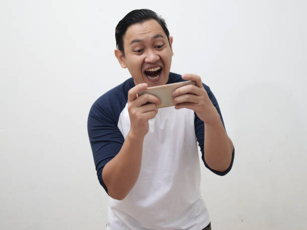 istock Asian man with funny face playing games on tablet smart phone 1338968859