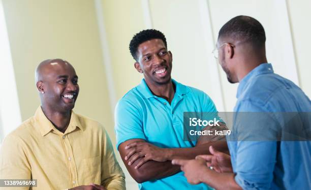 Three mid adult African-American men conversing indoors