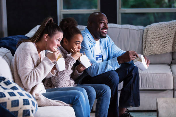 istock Multi-ethnic family on couch watching TV, eating takeout 1338970557