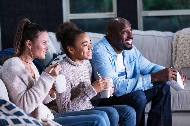 istock Multi-ethnic family on couch watching TV, eating takeout 1338970560