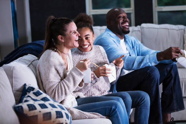 istock Multi-ethnic family on couch watching TV, eating takeout 1338970561