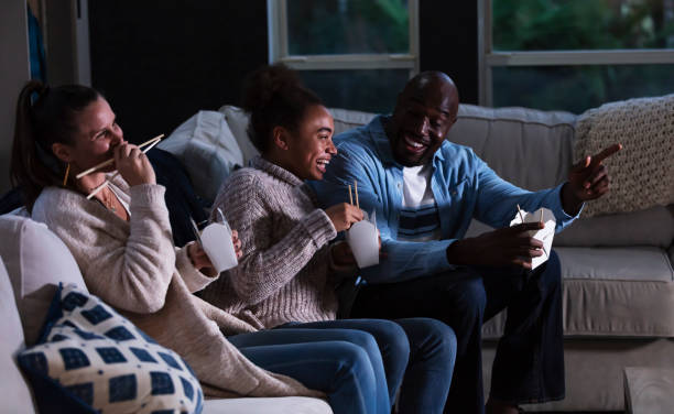 Multi-ethnic family on couch watching TV, eating takeout