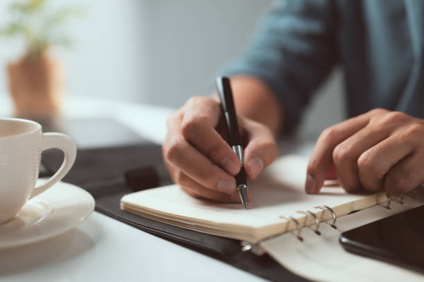 istock home office desk background, Hand holding pen and writing note on table, Checklist Notice Remember Planning Concept 1338973076