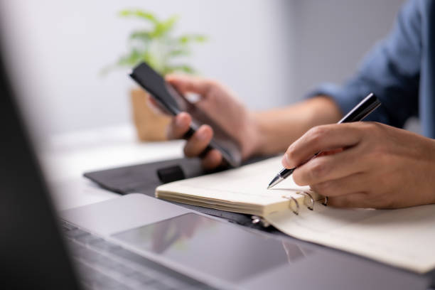 istock Hand holding pen and writing note on table. Checklist Notice Remember Planning Concept. Home office desk background 1338973149