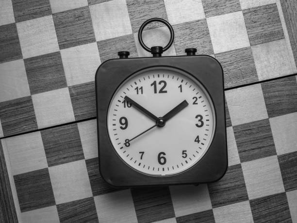 istock Black and white image of a classic clock on a chessboard. Flat lay. 1338973243