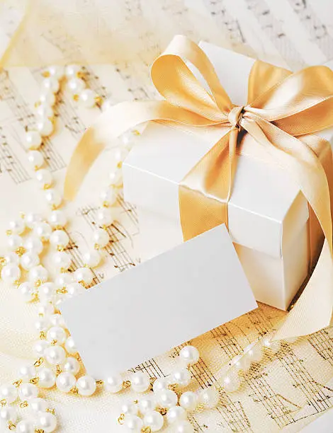 Gift box tied with gold ribbon with gift tag and pearl necklace on musical notes.