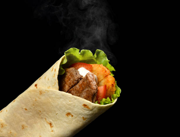 istock Classic tortilla wrap roll with grilled beef, cheese and vegetables, tomato, lettuce with steam smoke on black 1338982271