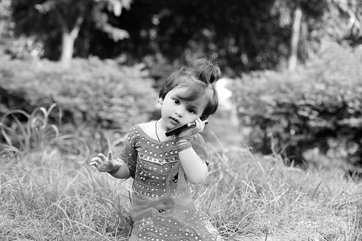 Sitting portrait of Radha little girl talking on mobile phone outdoors in public park, Delhi, India.