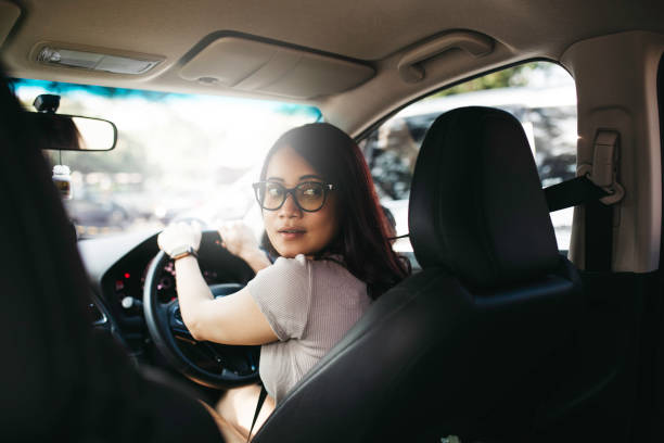 portrait d’une femme asiatique gare sa voiture et regardant en arrière en faisant marche arrière - car driving men reversing photos et images de collection