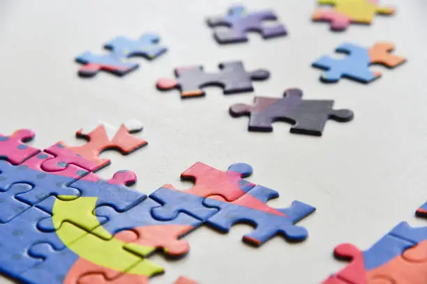 Selected focus on Fragment of a folded jigsaw puzzle and a pile of uncombed puzzle elements against the background of a white surface.