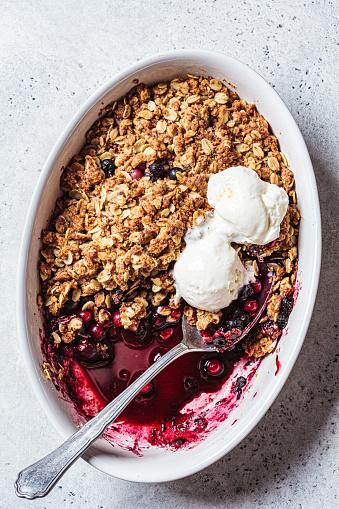Berry crumble pie in baking dish with a scoop of ice cream, gray background.