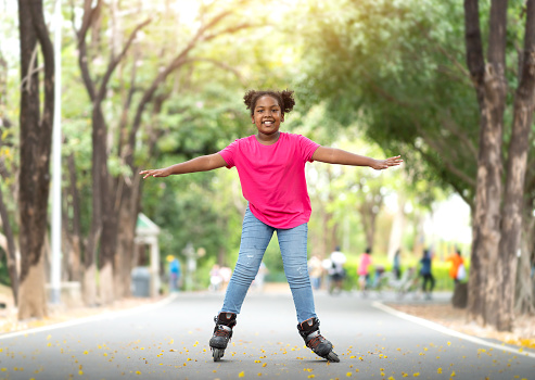 Cute African American little girl riding on roller skate in summer park. Kid enjoying outdoor sport in the park, Funny little girl playing on roller skate on road. sport learning outdoor concept
