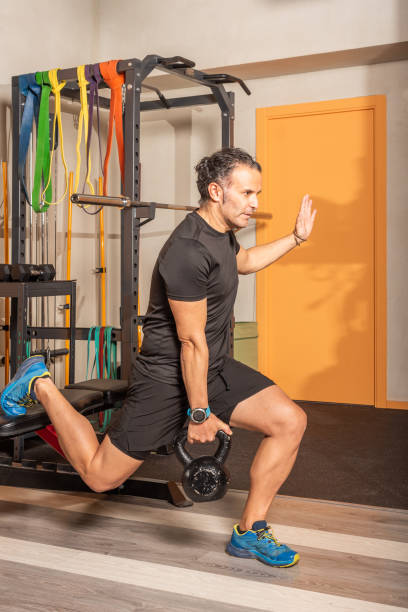 Man doing lunges with a kettlebells in her hand with one leg resting on a bench.