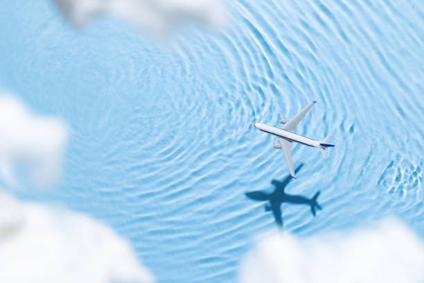Concept of a white airplane flying over blue water and clouds. Copy space, flat lay