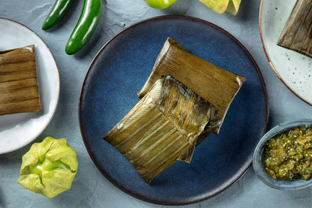 Tamales oaxaquenos, traditional dish of the cuisine of Mexico, Tamales oaxaquenos, traditional dish of the cuisine of Mexico, various stuffings wrapped in green leaves, overhead flat lay shot. Hispanic food. With chili peppers and tomatillos tomatillo photos stock pictures, royalty-free photos & images