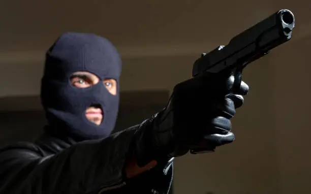 Murderer with balaclava concept. Blur criminal man in black hood leather jacket holds gun in gloved hand. Decided to implement action plan armed killer terrorist aiming with pistol weapon the target.