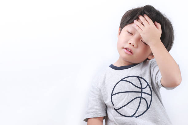 Portrait Of Confused Boy Against White Background Portrait Of A Little Asian Boy With Hand On His Forehead, Eyes Closed And Standing Against White Background sad child standing stock pictures, royalty-free photos & images