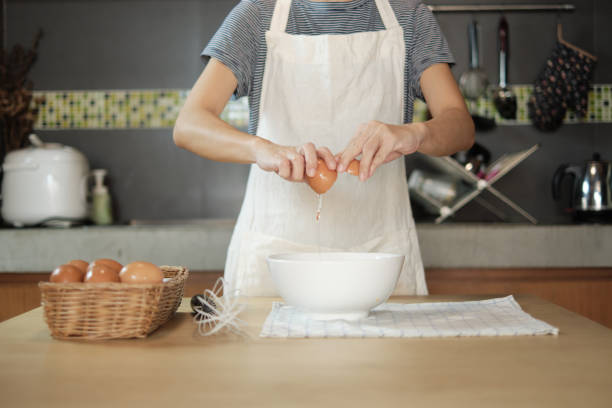 istock Female cook in a white apron is cracking an egg in home's kitchen. 1338996620