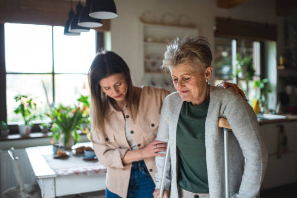 fille adulte rendant visite à une mère âgée malade avec des béquilles à l’intérieur de la maison, la tenant dans ses tenons. - crutch photos et images de collection