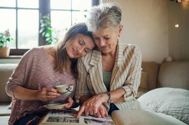 Senior mother with adult daughter indoors at home, looking at family photographs. A senior mother with adult daughter indoors at home, looking at family photographs. photograph album stock pictures, royalty-free photos & images