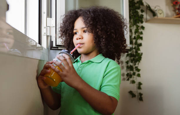 istock little afro boy drinks juice with straw at home at the window 1338999437