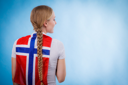 Blonde girl braid hair with norwegian flag on her back, copy space text area. Scandinavian people.