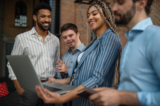 jóvenes empresarios alegres con laptop trabajando en oficina, inclusión social y concepto de cooperación. - lugar de trabajo fotografías e imágenes de stock