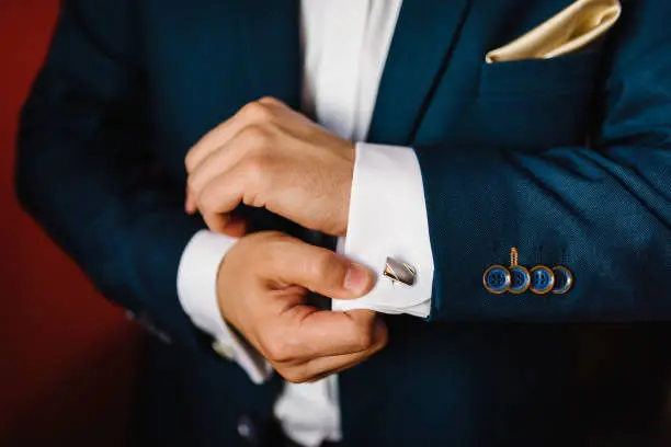 Man's hands buttoning cufflinks on white shirt. Groom's elegant male gold cufflink. wedding preparation morning of the groom. Close up.