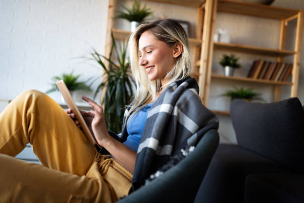 istock Relaxed young woman in sofa smiling content, happy and reading, working on tablet pc at home 1339001844