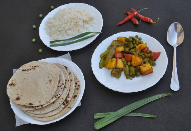istock Rice, matar paneer mix veg and roti (Indian bread) on white plate over black background 1339002249